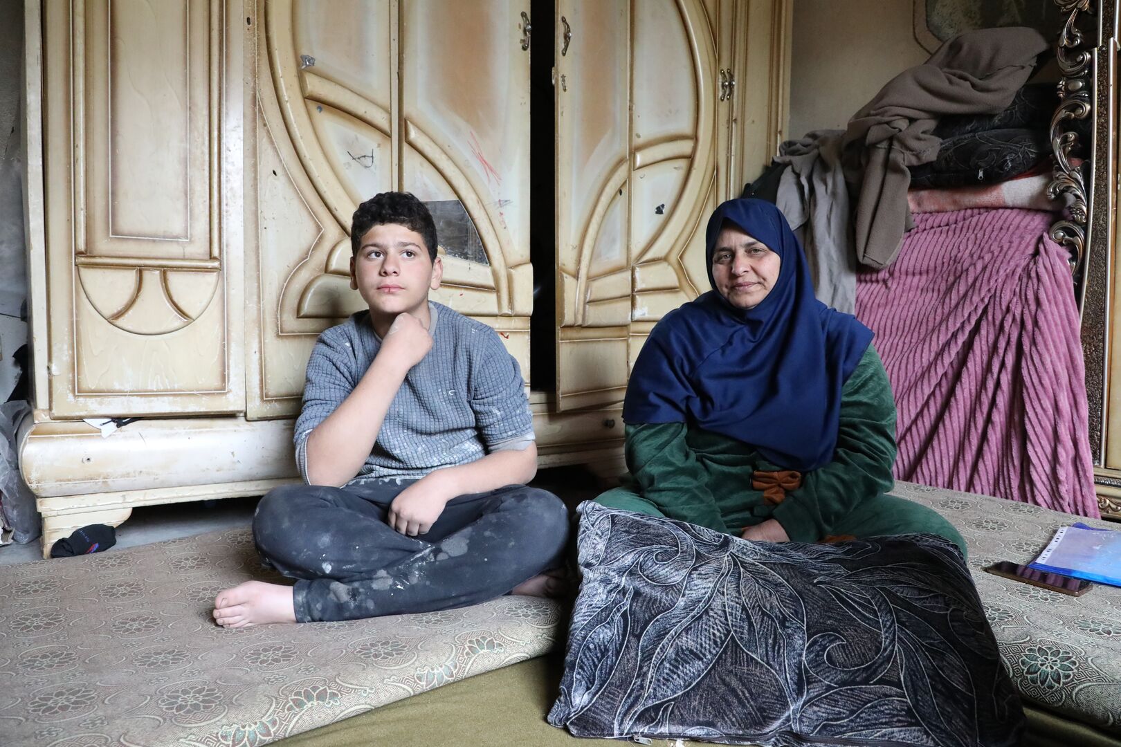 Syrian refugee returnee Ibtihal, 52, a mother of five, and her youngest son, Omar, 14, sit in their damaged house in Sheikh Miskeen, Dar’a governorate, Syria